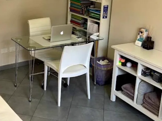 Lo studio di Vignate presso Fisiomed dove riceve la Dott.ssa Laura Roca: scrivania in vetro con computer portatile e libreria
